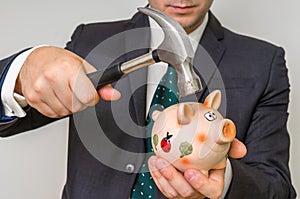 Hopeless businessman breaking piggy bank with hammer