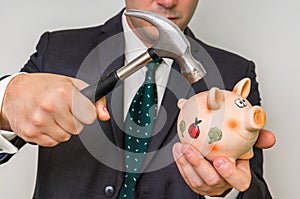 Hopeless businessman breaking piggy bank with hammer