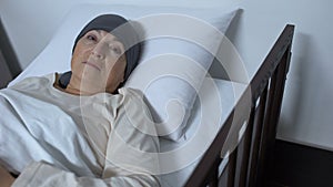 Hopeless female patient suffering cancer lying in sickbed and looking at camera