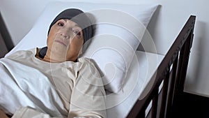 Hopeless female patient suffering cancer lying in sickbed and looking at camera