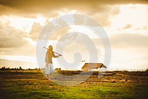 Hopeless and lonely Farmer carrying hoe and walking through his dry field at sunset. Global warming crisis