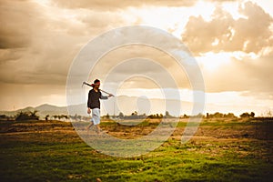 Hopeless and lonely Farmer carrying hoe and walking through his dry field at sunset. Global warming crisis