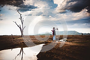 Hopeless and lonely farmer sit on cracked earth near drying water