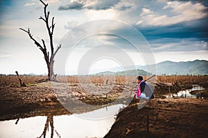 Hopeless and lonely farmer sit on cracked earth near drying water