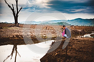 Hopeless and lonely farmer sit on cracked earth near drying water