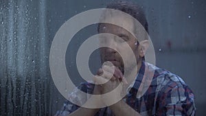 Hopeless male praying God behind rainy window, asking for help and forgiveness