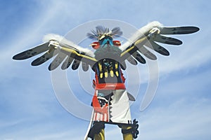Hopi Kachina doll with outstretched winged arms against blue sky