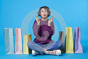 Hoping young attractive curly brunette woman raising hands with crossed fingers and biting underlip while looking worringly