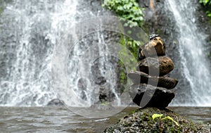 Horisontal shot of rocks perfectly balanced on top of each other in front of a waterfall in a forest