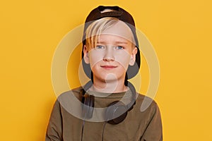Horixontal shot of little blond boy with headphones around neck, male child listening to music via headphones, wearing green shirt