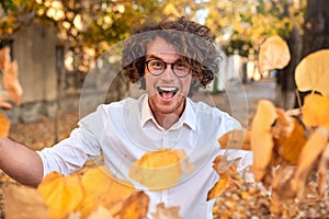 Horizontal autumn shot of happy handsome winner young man with glasses playing with leaves outdoors.Successful male student enjoy