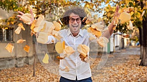 Horizontal autumn shot of happy handsome winner young man with glasses playing with leaves outdoors.Successful male student enjoy