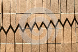 Horizontal background of notched shadow of the grate on the brown floor tiles with small dents, scratches and bumps