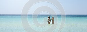 Horizontal banner or header with back view of two beautiful friendly women bathing in the clear sea against a sunny sky. Vacation
