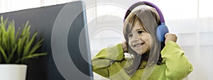 Horizontal banner or header with elementary schooler girl in headphones sitting at desk on laptop - Cute girl studying online from