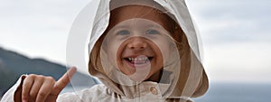 Horizontal banner or header with a little smiling girl wearing a raincoat jacket with hood against the stormy sky - She lifts her