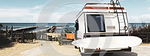 Horizontal banner or header with rear view of vintage camper parked on the beach against a scenic view - Caravan of surfer with a