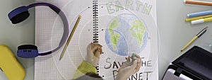 Horizontal banner or header with top view of child girl draws planet earth with wax colors on school notebook for Earth day -