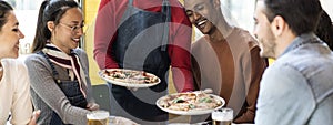 Horizontal banner or header with waiter serving delicious pizzas margherita to multicultural friends in cozy pizzeria restaurant