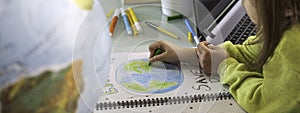 Horizontal banner or header with wide angle view of child girl draws planet earth with wax colors on school notebook for Earth day