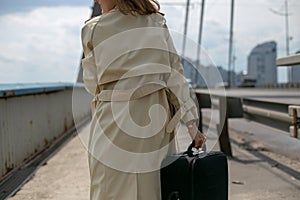 Horizontal close-up photo from the back of a young woman in a raincoat on a bridge
