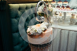 Horizontal close-up shot of the beautiful orange wedding cake decorated with white and beige flowers and hanging beads.