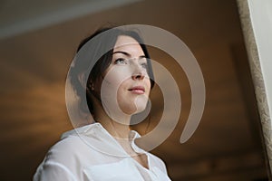 Horizontal closeup portrait of a beautiful brunette in a white blouse near a window