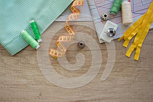 Horizontal composition with threads and sewing accessories and tools in green and yellow colours, on wooden background with copy