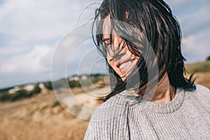 Horizontal cropped portrait of beautiful smiling woman wearing sweater being playful with windy hair and carefree posing on