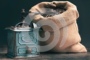 Horizontal detail straight studio shot of still life with vintage manual green metal coffee grinder, jute bag and coffee