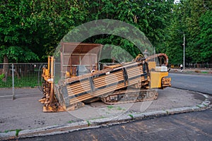 Horizontal Directional Drill. The orange drilling rig stands on the city square. Dark asphalt and trees in the background