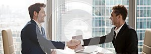 Horizontal image businessmen in suits handshaking sitting at office desk