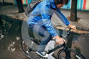 Horizontal image of a handsome man cycling on his bike down the street next to the house. Male courier with curly hair delivers