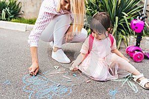 Horizontal image of happy little girl and mother drawing with chalks on sidewalk. Caucasian female play together with kid