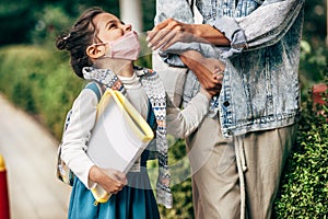 Horizontal image of a kid wearing protective face mask going back to the school with her mother during coronavirus. Happy little