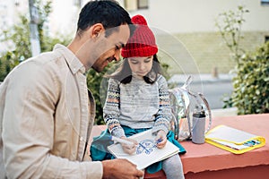 Horizontal image of pretty little girl in red cap drawing with her dad together outdoors after school. Father enjoying the time