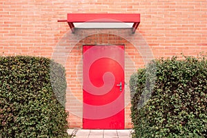 Horizontal image. Red door surrounded by orange brick wall.