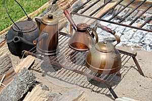 Horizontal image of several cast iron and copper kettles on open fire pit