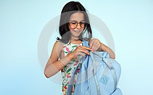 Horizontal image of a smiling little girl wearing summer dress preparing her backpack in the morning for the school summer camp