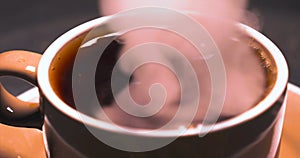 Horizontal image of white antique cup of black coffee sitting on railing with steam rising up with background black. Colorful hand