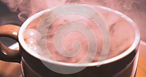 Horizontal image of white antique cup of black coffee sitting on railing with steam rising up with background black. Colorful hand