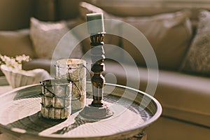 Horizontal image of wooden and glass candleholders on a round coffee table in a cozy home interior.