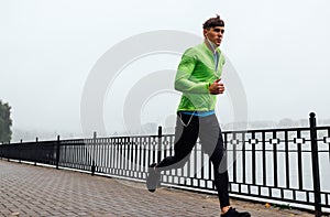 Horizontal image of young athelte man running in the morning on the fog lake background. Fitness male exercising in the park and