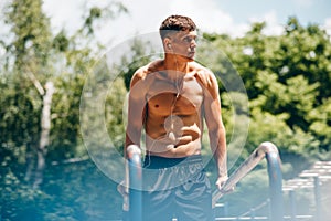 Horizontal image of young fitness muscular man doing exercises on horizontal crossbar at sportsground. Handsome athletic shirtless