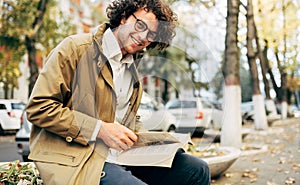 Horizontal image of a young man reading a book outdoors. College male student learns on campus in the autumn street. Smiling smart