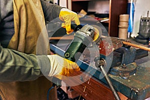Horizontal indoor image of adult worker man manufacturing in his workshop. Carpenter male grinding with sparks in repair shop