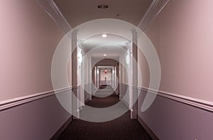 Horizontal interior view of the hallway of a modern apartment building; with sconces, doorways, molding, lighting  and carpeting