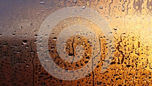 Horizontal natural background with water drops on the window with sunbeams, condensation on the glass with dripping drops