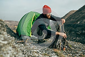 Horizontal outdoors image of young hiker male prepare brunches for bonfire in mountains.