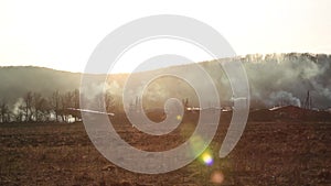 Horizontal panorama, burning grass near forest with lots of smoke next to wooden houses at sunset against mountain